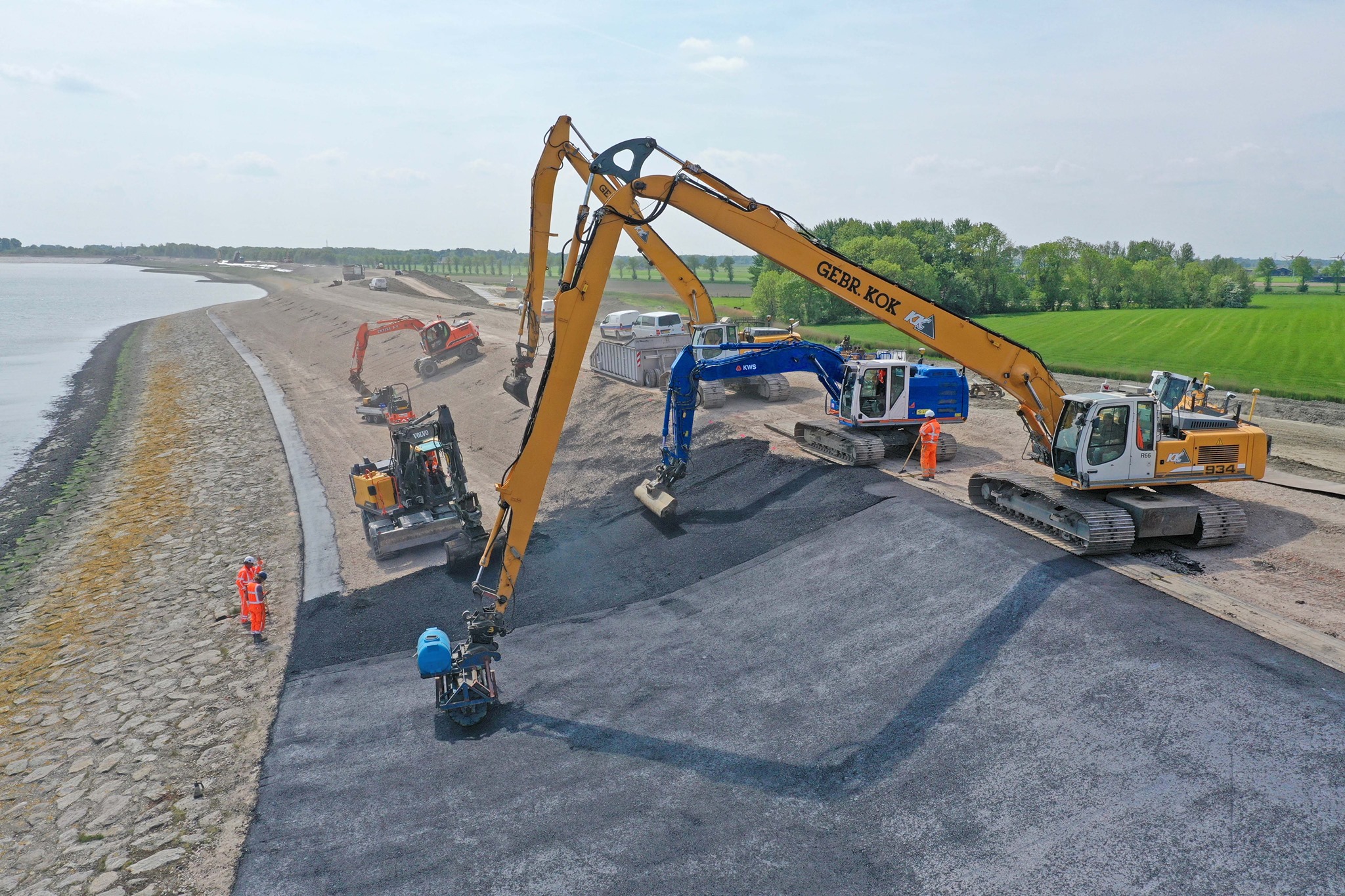 Een weergave van een situatie waar een hydraulische graafmachine waterbouwasfalt aanbrengt.